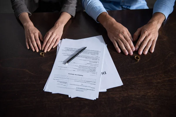 Vue partielle du couple à table avec documents de divorce et anneaux — Photo de stock