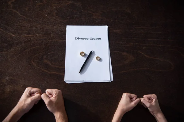 Partial view of couple clenching fists at table with divorce documents and rings — Stock Photo