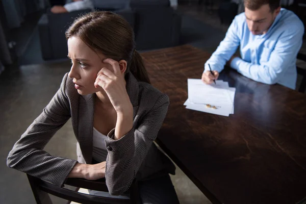 Triste femme coûteuse regardant loin et homme signer des documents à table — Photo de stock