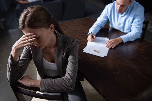 Triste femme coûteuse touchant le front et l'homme signer des documents à table — Photo de stock