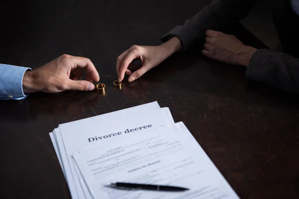 Vue partielle du couple à table avec documents de divorce et anneaux — Photo de stock