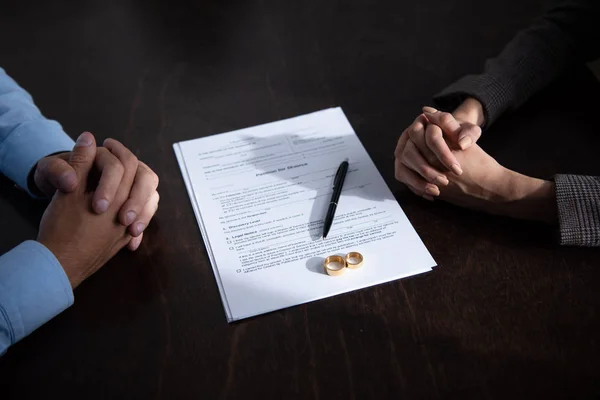 Vue partielle du couple assis à table les mains serrées près des documents de divorce et des anneaux — Photo de stock