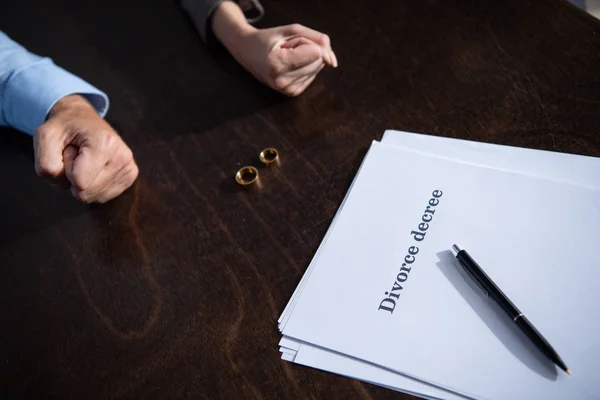 Cropped view of couple with clenched fists sitting at table with rings — Stock Photo