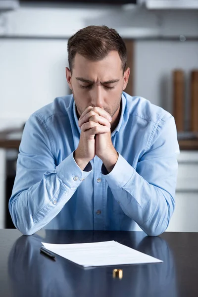 Homme triste en chemise assis à table avec bague et documents de divorce — Photo de stock