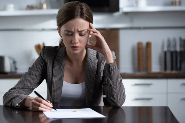 Upset woman in jacket sitting at table and signing divorce document — Stock Photo