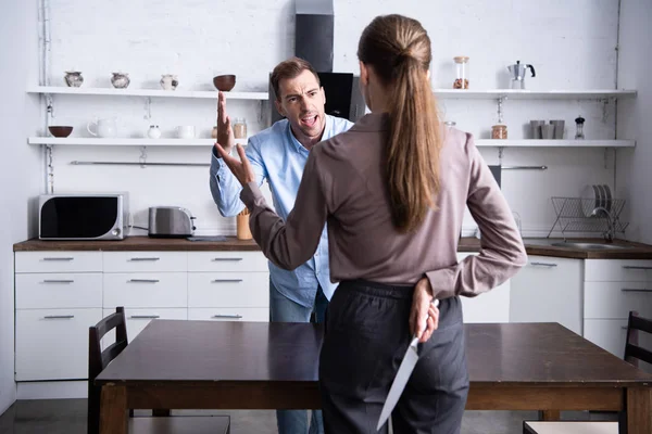 Back view of woman holding knife while husband yelling at her during quarrel — Stock Photo