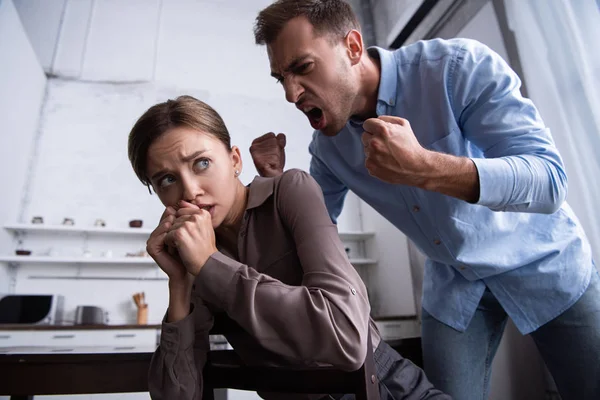 Агрессивный мужчина держит кулаки и кричит на испуганную жену — стоковое фото