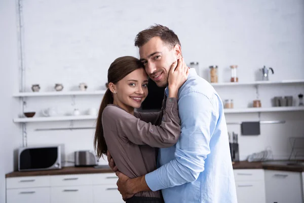 Moglie sorridente e marito che abbraccia in cucina a casa — Foto stock