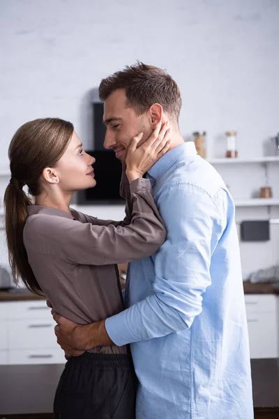 Vista lateral da esposa e do marido abraçando na cozinha em casa — Fotografia de Stock