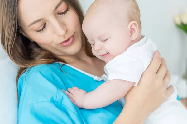 Attractive and young mother holding her child in hospital — Stock Photo