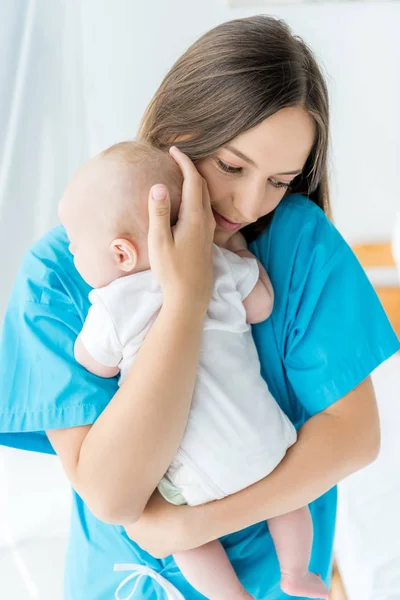 Attractive and young mother holding her child in hospital — Stock Photo