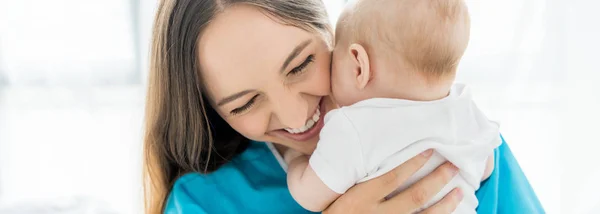 Panoramic shot of attractive and smiling mother holding her child in hospital — Stock Photo