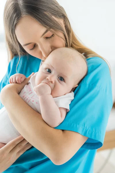 Attractive mother kissing and holding her child in hospital — Stock Photo