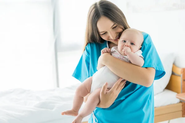 Attractive and young mother holding her child in hospital — Stock Photo