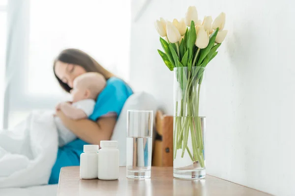 Selective focus of attractive and young mother holding her child in hospital — Stock Photo
