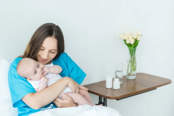 Attractive and young mother holding her child in hospital — Stock Photo