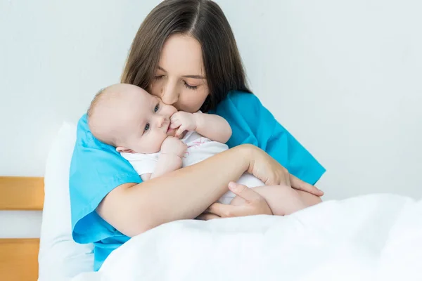 Attrayant et jeune mère tenant et embrassant son enfant à l'hôpital — Photo de stock
