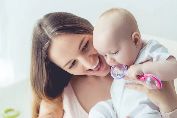 Atractiva y sonriente madre sosteniendo a su hijo en el apartamento - foto de stock