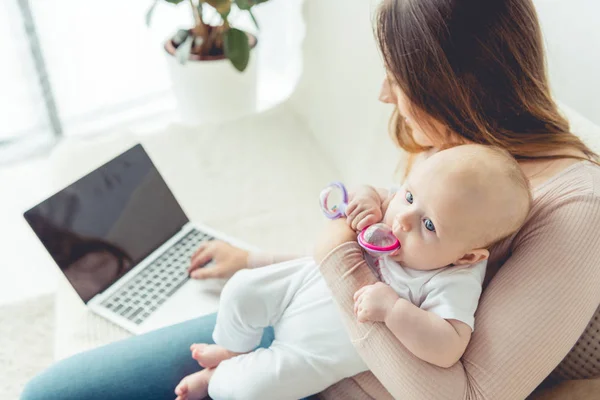 Mutter hält ihr Kind und benutzt Laptop mit Kopierplatz in Wohnung — Stockfoto