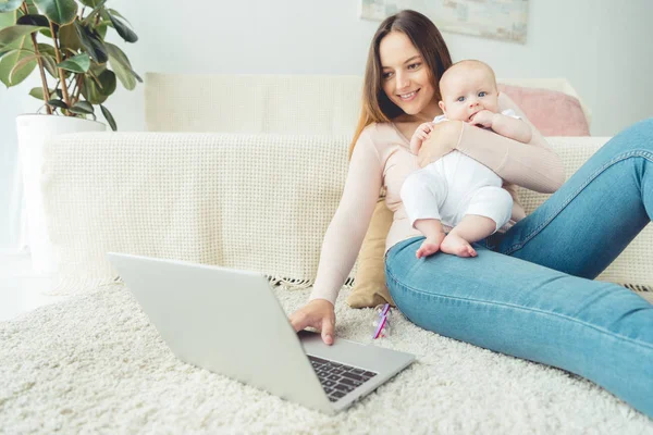 Mãe atraente segurando seu filho e usando laptop no apartamento — Fotografia de Stock