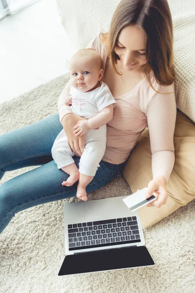 Attraktive Mutter hält ihr Kind und ihre Kreditkarte in der Wohnung — Stockfoto