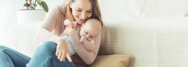 Panoramic shot of attractive mother holding her child and pointing with finger in apartment — Stock Photo