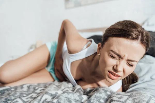 Stressed woman lying on bed and touching belly with closed eyes — Stock Photo