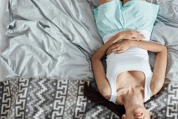 Partial view of young woman lying on bed and touching belly — Stock Photo