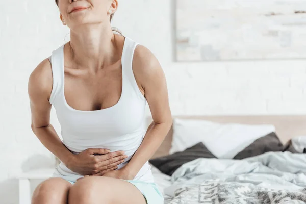 Partial view of young woman sitting on bed and touching belly — Stock Photo