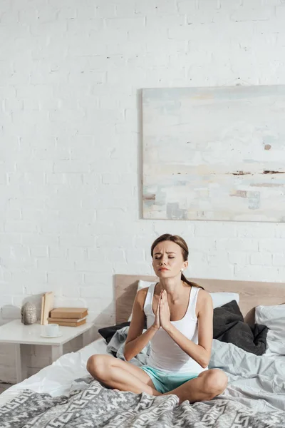 Chateado jovem mulher sentada na cama com os olhos fechados e mostrando por favor gesto — Fotografia de Stock