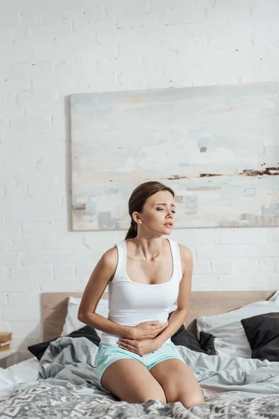 Stressato giovane donna seduta sul letto e toccante pancia — Foto stock