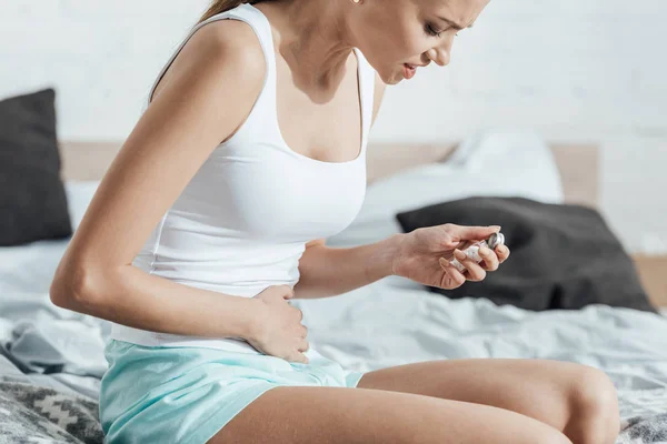 Teilbild einer Frau, die Tabletten in der Hand hält und Bauch berührt — Stockfoto