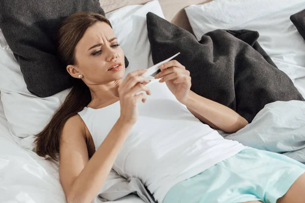 Mujer joven preocupada sosteniendo prueba de embarazo en la cama - foto de stock