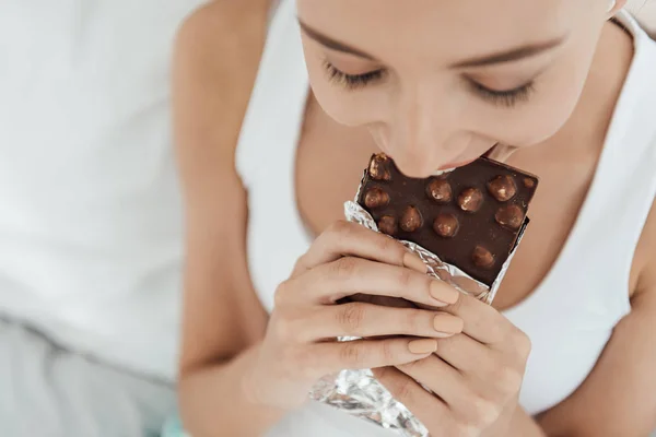 Overhead view of young woman eating chocolate with nuts in bed — Stock Photo