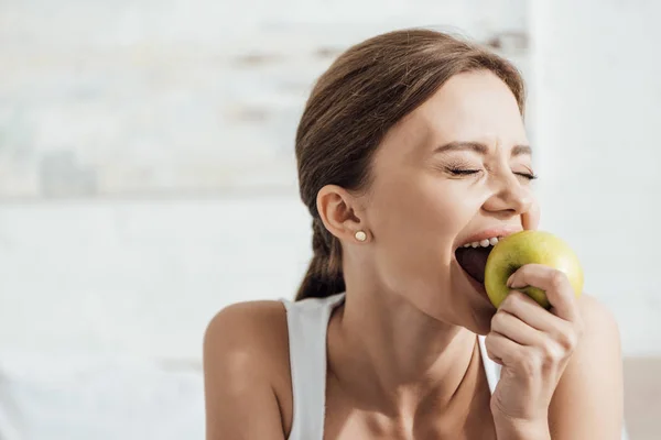 Attractive young woman eating green apple with closed eyes — Stock Photo