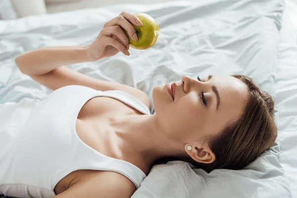 Attractive young woman holding green apple in bed — Stock Photo