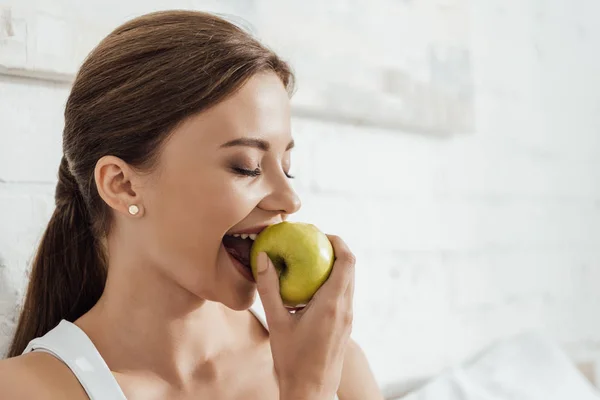 Attraktive junge Frau isst grünen Apfel im Bett — Stockfoto