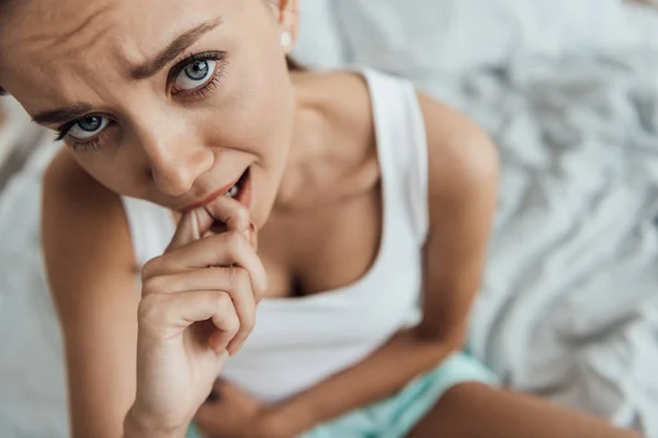 Blick von oben auf gestresste junge Frau, die auf dem Bett sitzt und den Bauch berührt — Stockfoto