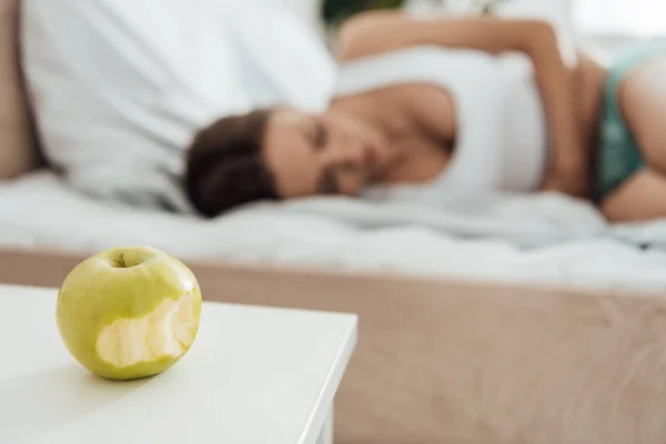 Selective focus of suffering woman touching belly and green apple on foreground — Stock Photo