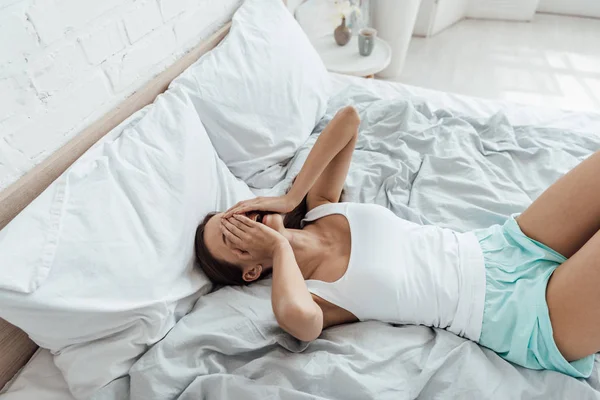 Напружена молода жінка вкриває обличчя руками і плаче в ліжку — стокове фото