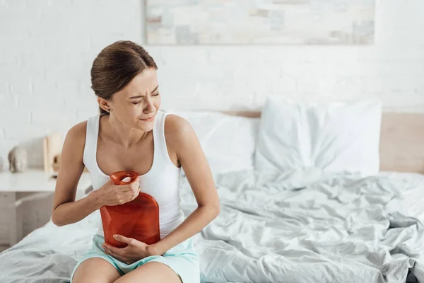 Mujer joven estresada sentada en la cama y sosteniendo más caliente - foto de stock