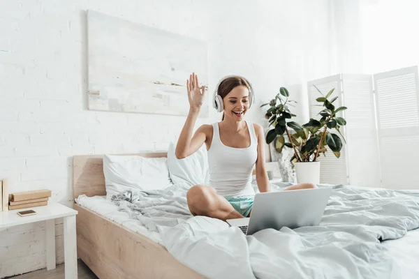 Young woman listening music in headphones and using laptop on bed — Stock Photo