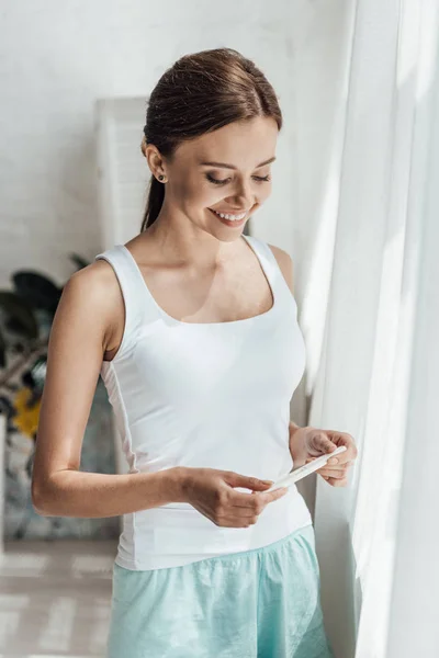 Усміхнена молода жінка тримає тест на вагітність вдома — стокове фото