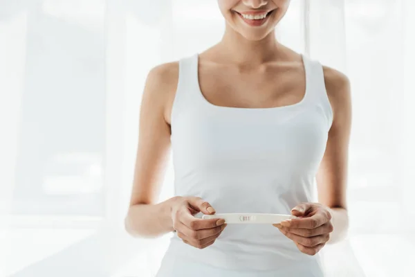 Обрізаний вид усміхненої молодої жінки, що тримає тест на вагітність вдома — стокове фото