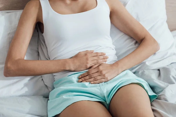 Vista parcial de la chica acostada en la cama y tocando el vientre - foto de stock