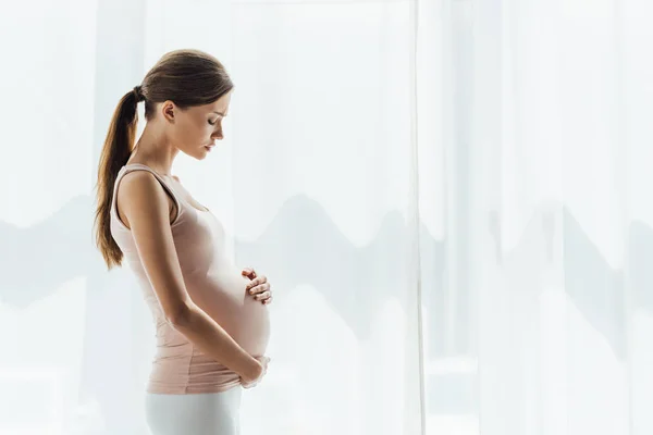 Vista lateral de la mujer embarazada tocando el vientre con los ojos cerrados - foto de stock