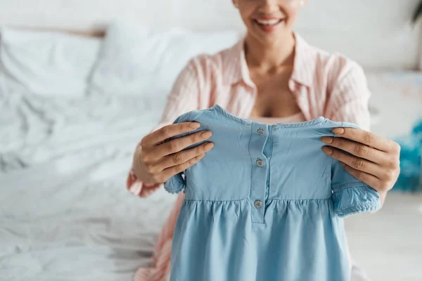 Vista recortada de la mujer sonriente sosteniendo ropa de bebé - foto de stock