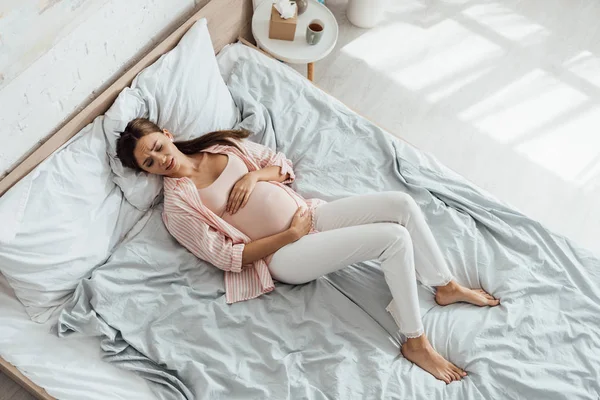 Vista aérea de la triste mujer embarazada acostada en la cama y tocando el vientre - foto de stock