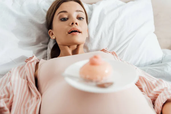 Vista de ángulo bajo de la mujer embarazada acostada en la cama con cupcake dulce - foto de stock