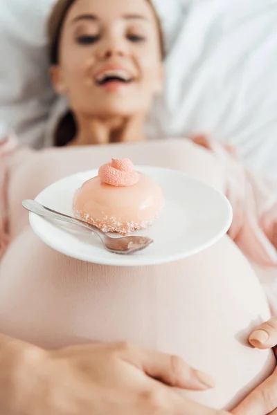 Selective focus of pregnant woman lying in bed with cupcake — Stock Photo